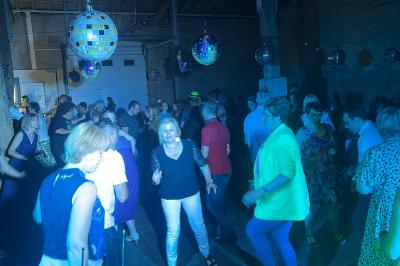 Des personnes dansent dans une salle éclairée par des lumières rouges, entourées de tables dressées pour un événement.