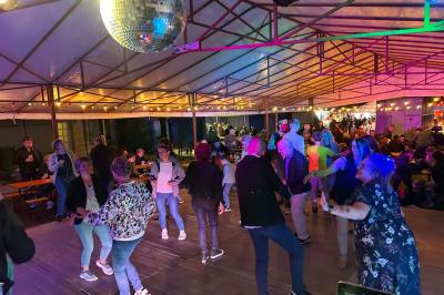 Des personnes dansent dans une salle éclairée par des lumières rouges, entourées de tables dressées pour un événement.