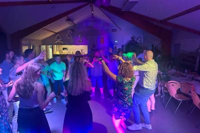 Des personnes dansent dans une salle éclairée par des lumières rouges, entourées de tables dressées pour un événement.