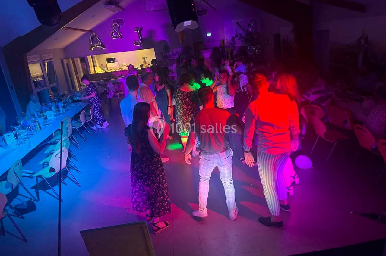 Des personnes dansent sous des lumières colorées dans une salle décorée, avec des tables disposées sur les côtés.