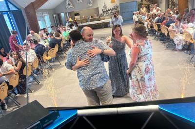 Des personnes dansent dans une salle éclairée par des lumières rouges, entourées de tables dressées pour un événement.