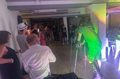 Des personnes dansent dans une salle éclairée par des lumières rouges, entourées de tables dressées pour un événement.