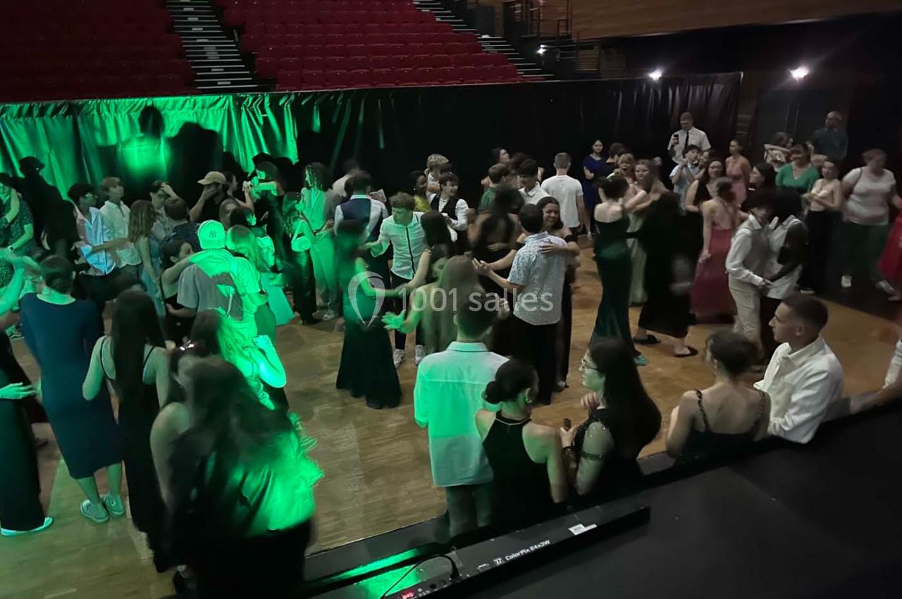 Des personnes dansent et discutent dans une salle de réception éclairée par des lumières vertes, avec des gradins en arrière…