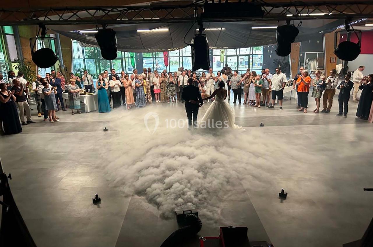 Un couple danse au centre d'une salle décorée, entouré de fumée au sol et d'invités observant la scène.