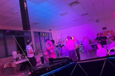 Des personnes dansent dans une salle éclairée par des lumières rouges, entourées de tables dressées pour un événement.