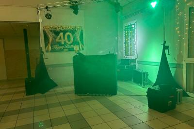 Des personnes dansent dans une salle éclairée par des lumières rouges, entourées de tables dressées pour un événement.