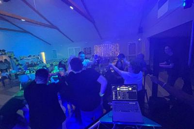 Des personnes dansent dans une salle éclairée par des lumières rouges, entourées de tables dressées pour un événement.