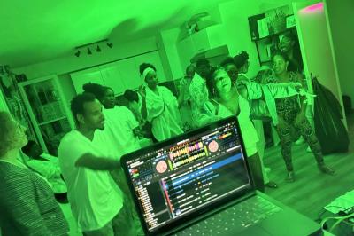 Des personnes dansent dans une salle éclairée par des lumières rouges, entourées de tables dressées pour un événement.