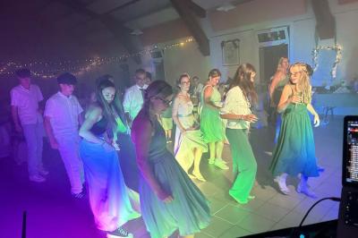 Des personnes dansent dans une salle éclairée par des lumières rouges, entourées de tables dressées pour un événement.