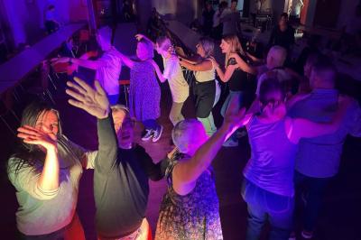 Des personnes dansent dans une salle éclairée par des lumières rouges, entourées de tables dressées pour un événement.