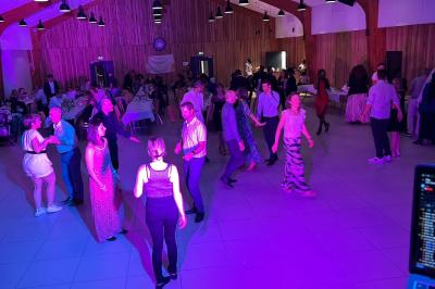 Des personnes dansent dans une salle éclairée par des lumières rouges, entourées de tables dressées pour un événement.