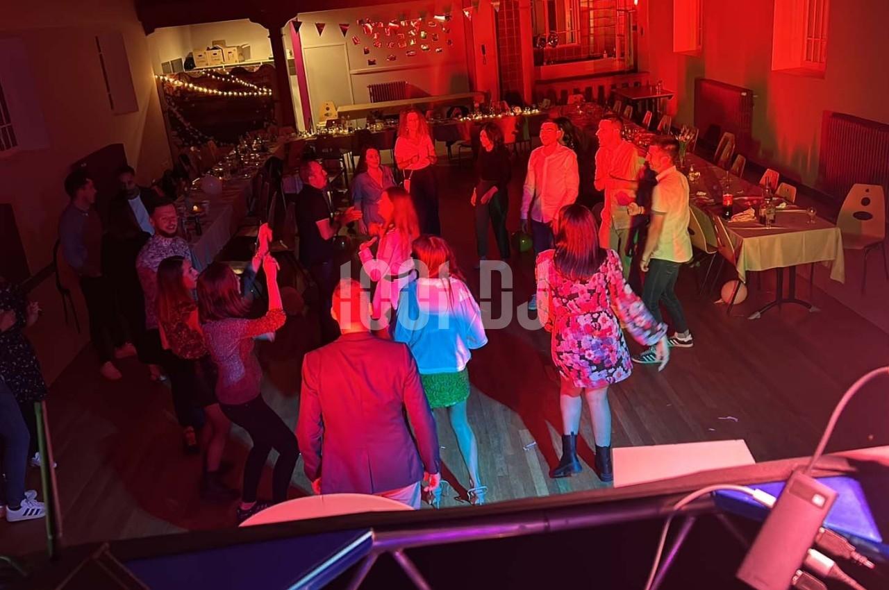 Des personnes dansent dans une salle éclairée par des lumières rouges, entourées de tables dressées pour un événement.