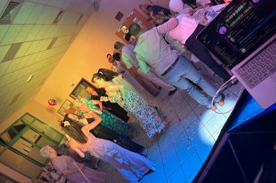 Des personnes dansent dans une salle éclairée par des lumières rouges, entourées de tables dressées pour un événement.