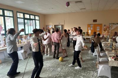 Des personnes dansent dans une salle éclairée par des lumières rouges, entourées de tables dressées pour un événement.