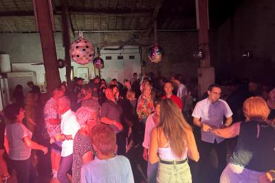 Des personnes dansent dans une salle éclairée par des lumières rouges, entourées de tables dressées pour un événement.
