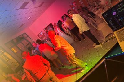 Des personnes dansent dans une salle éclairée par des lumières rouges, entourées de tables dressées pour un événement.