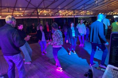 Des personnes dansent dans une salle éclairée par des lumières rouges, entourées de tables dressées pour un événement.
