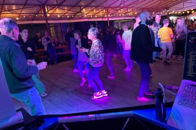 Des personnes dansent dans une salle éclairée par des lumières rouges, entourées de tables dressées pour un événement.