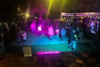 Des personnes dansent dans une salle éclairée par des lumières rouges, entourées de tables dressées pour un événement.