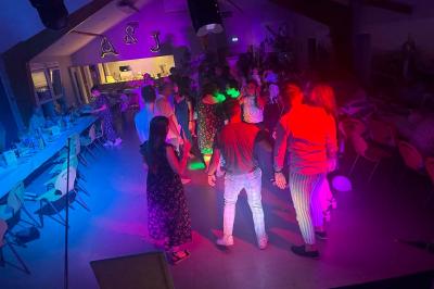 Des personnes dansent dans une salle éclairée par des lumières rouges, entourées de tables dressées pour un événement.