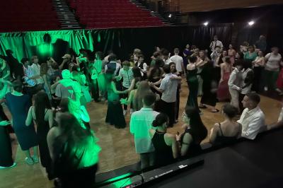 Des personnes dansent dans une salle éclairée par des lumières rouges, entourées de tables dressées pour un événement.