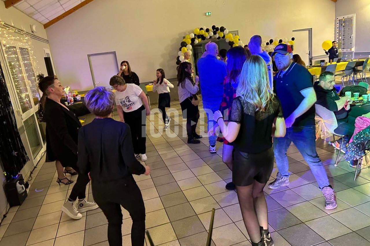 Des personnes dansent et discutent dans une salle décorée de ballons noirs et jaunes, éclairée par des lumières festives.