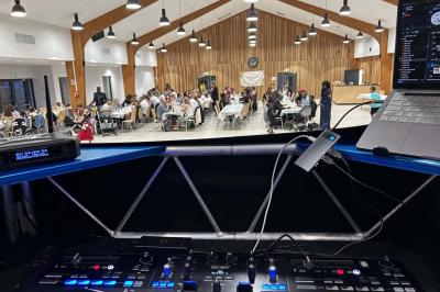 Des personnes dansent dans une salle éclairée par des lumières rouges, entourées de tables dressées pour un événement.