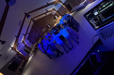 Des personnes dansent dans une salle éclairée par des lumières rouges, entourées de tables dressées pour un événement.