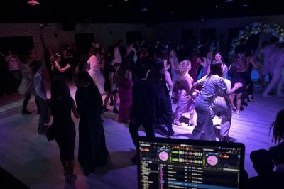 Des personnes dansent dans une salle éclairée par des lumières rouges, entourées de tables dressées pour un événement.