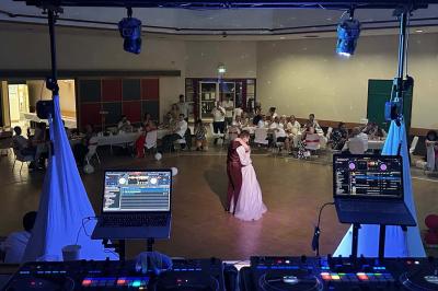 Des personnes dansent dans une salle éclairée par des lumières rouges, entourées de tables dressées pour un événement.
