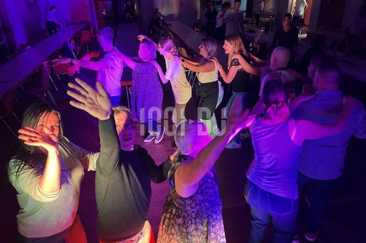 Des personnes dansent en groupe dans une salle éclairée par des lumières colorées, créant une ambiance festive.