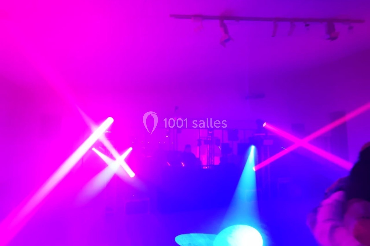 Salle plongée dans une ambiance lumineuse rose et violette avec des faisceaux de projecteurs et une silhouette floue.
