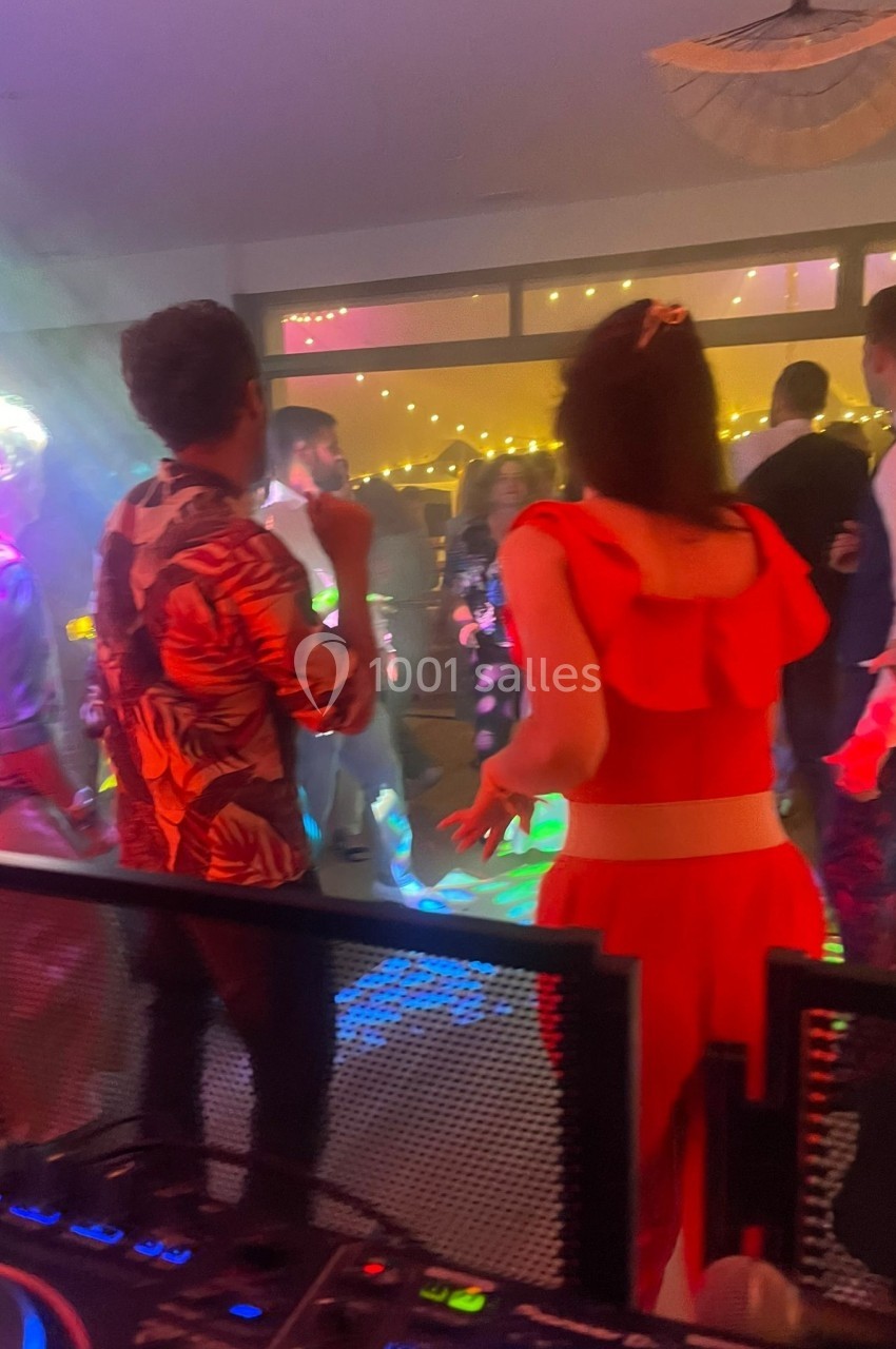 Des personnes dansent dans une ambiance festive avec des lumières colorées, vue depuis une table de mixage.