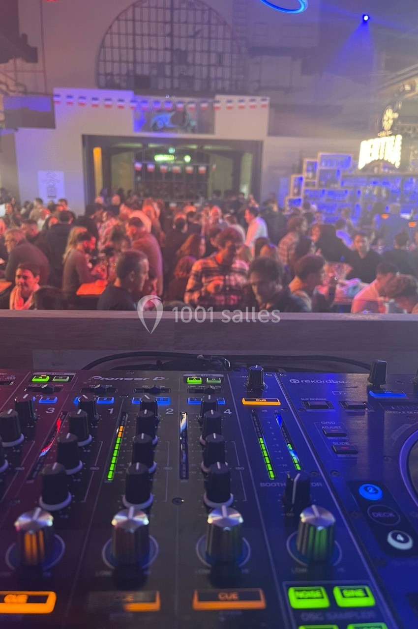 Vue d'une table de mixage en premier plan avec une salle animée et des convives en arrière-plan.