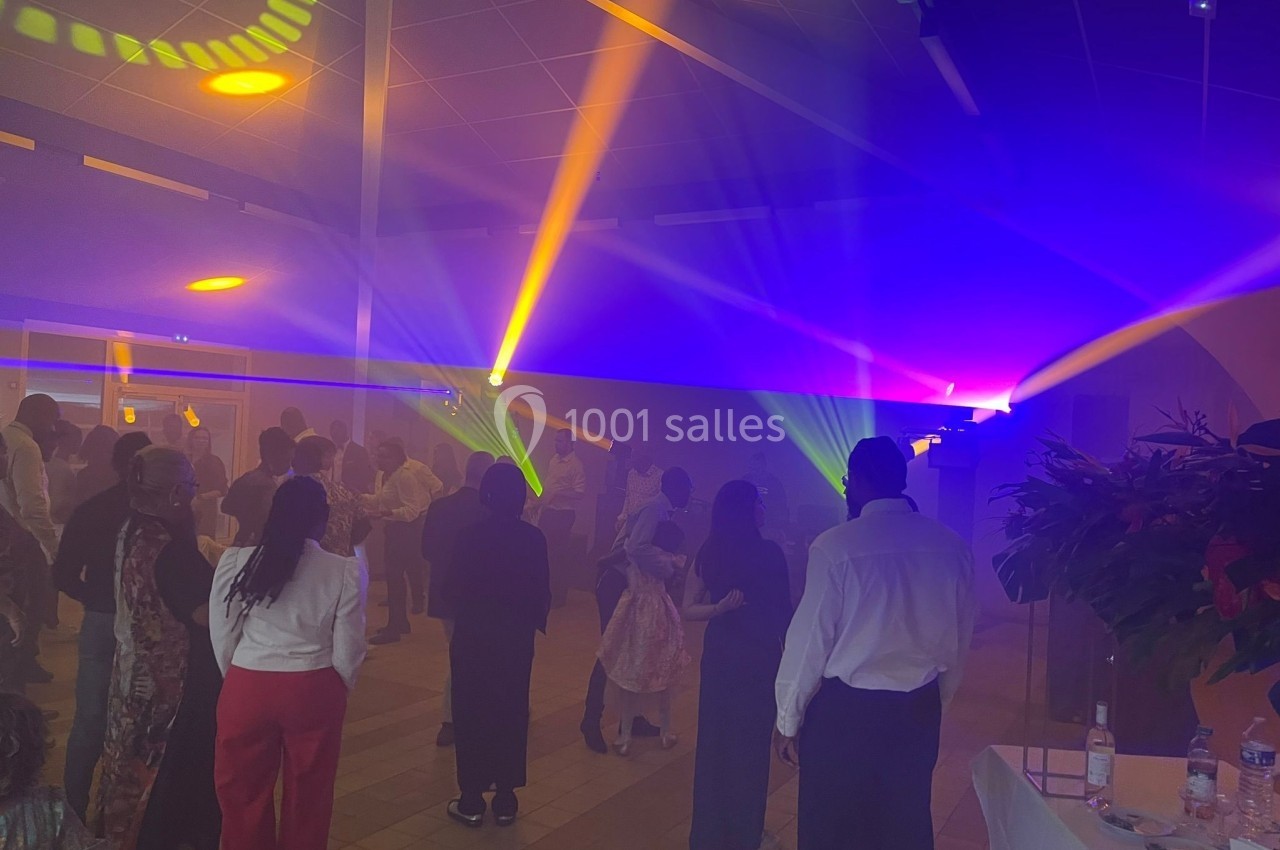 Des personnes dansent dans une salle éclairée par des jeux de lumière colorés, avec une ambiance festive.