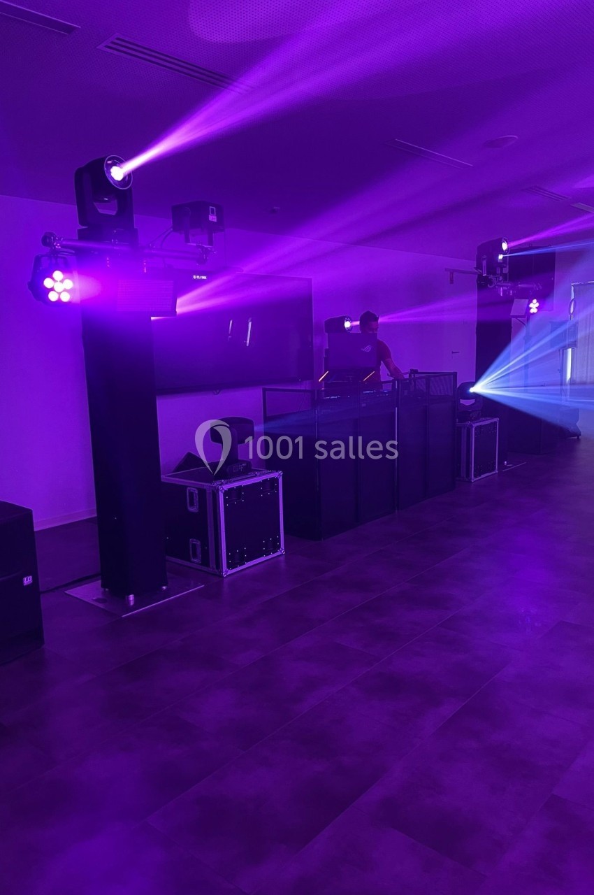 Salle sombre avec éclairage violet, un DJ derrière une table de mixage et des projecteurs diffusant des faisceaux lumineux.