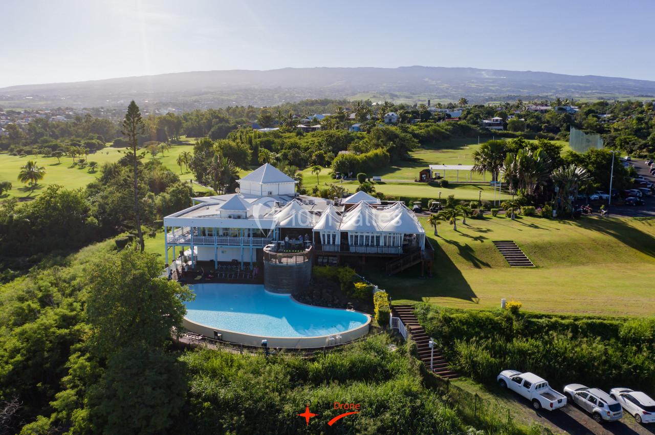 Vue aérienne d'un bâtiment avec piscine à débordement, entouré de verdure et situé près d'un terrain de golf.