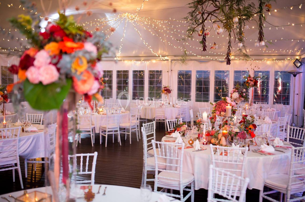 Salle de réception décorée avec des guirlandes lumineuses, des tables élégantes et des arrangements floraux colorés.