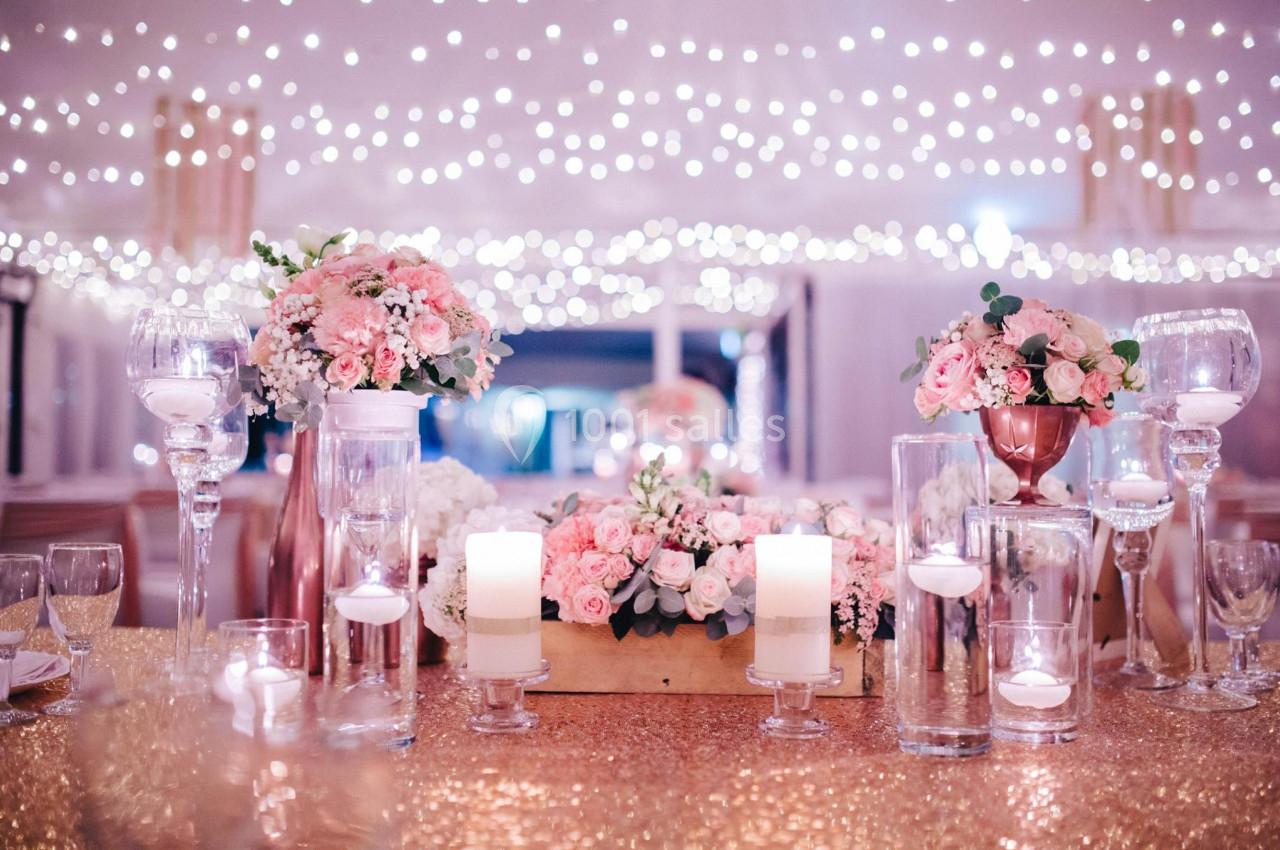 Décoration de table élégante avec bougies, fleurs roses et blanches, sous un plafond illuminé de guirlandes lumineuses.