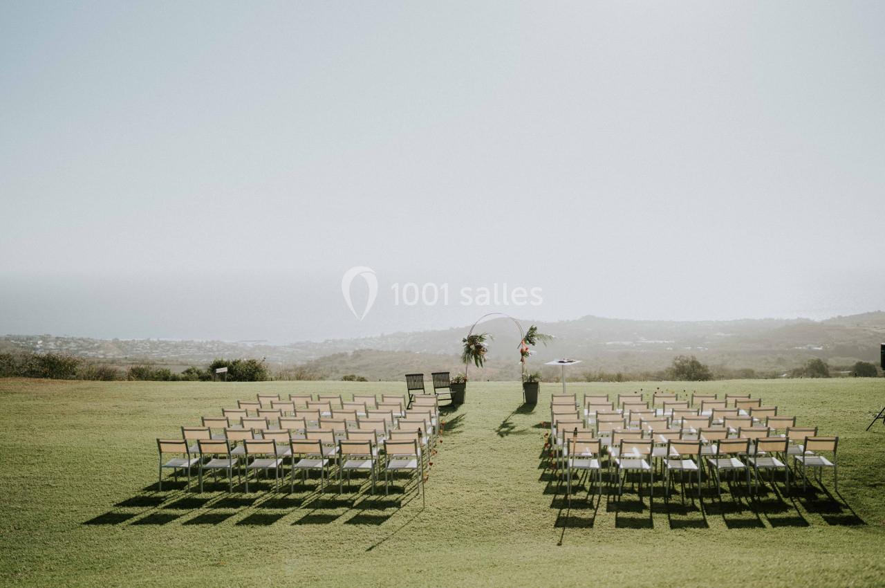 Chaises alignées en extérieur sur une pelouse, face à une arche décorée pour une cérémonie avec vue sur un paysage dégagé.