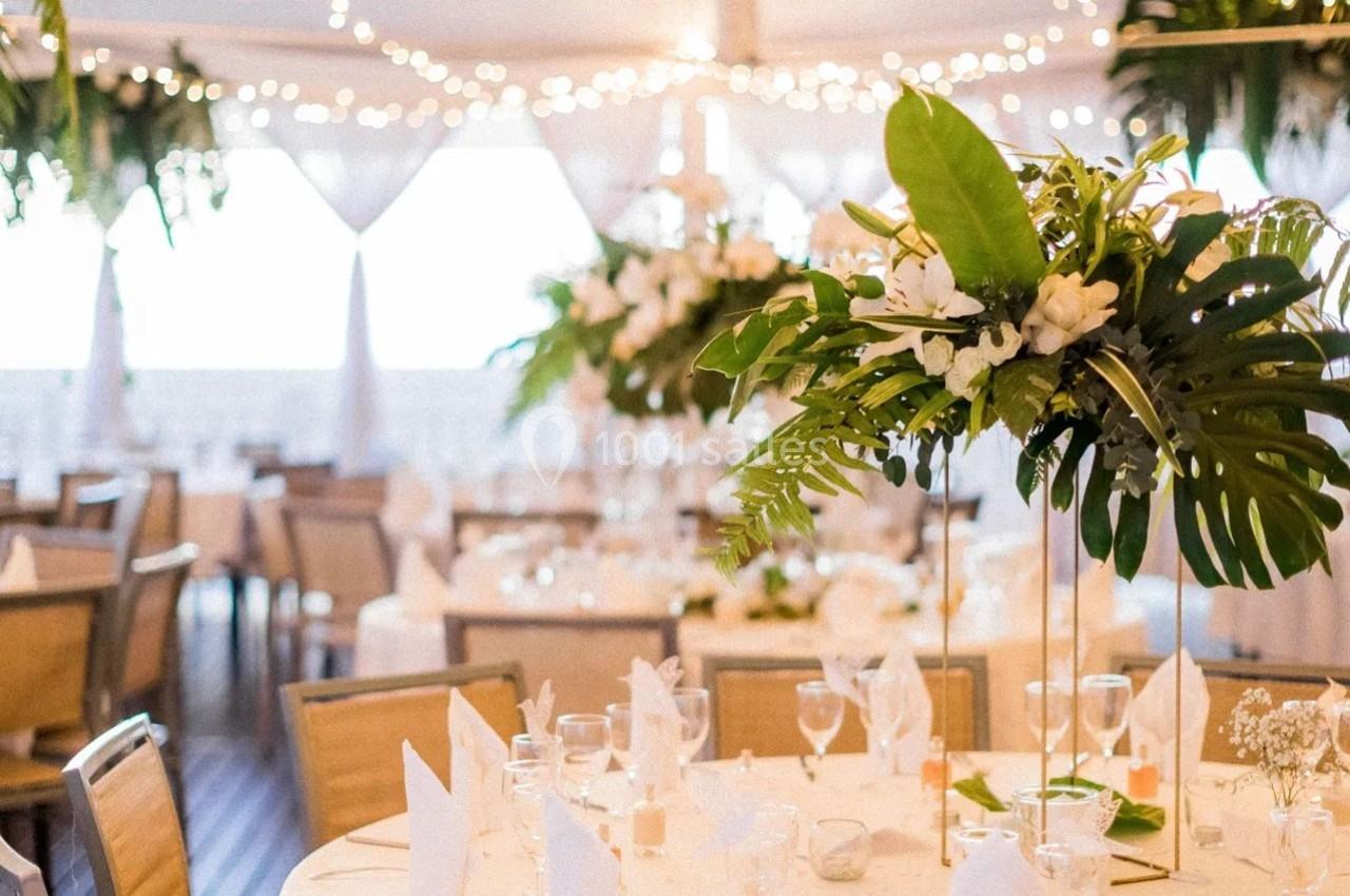 Salle de réception décorée avec des tables rondes, des nappes blanches et des centres de table floraux élégants.