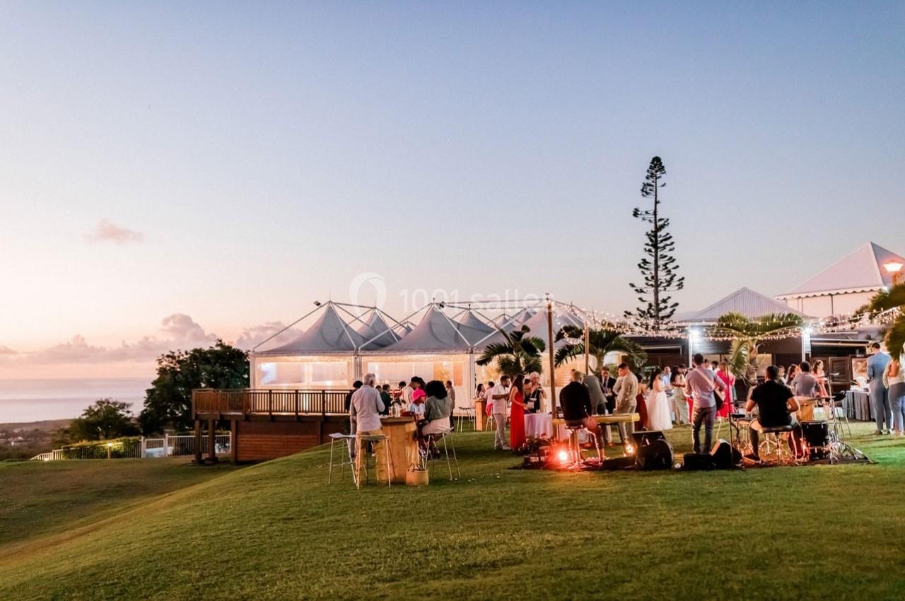 Groupe de personnes rassemblées sur une pelouse au coucher du soleil, près de structures légères et éclairées.