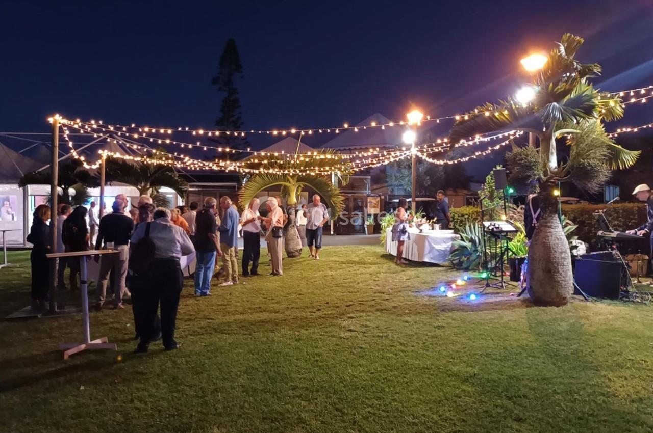 Groupe de personnes rassemblées dans un jardin éclairé par des guirlandes lumineuses, près de tables et d'un buffet.