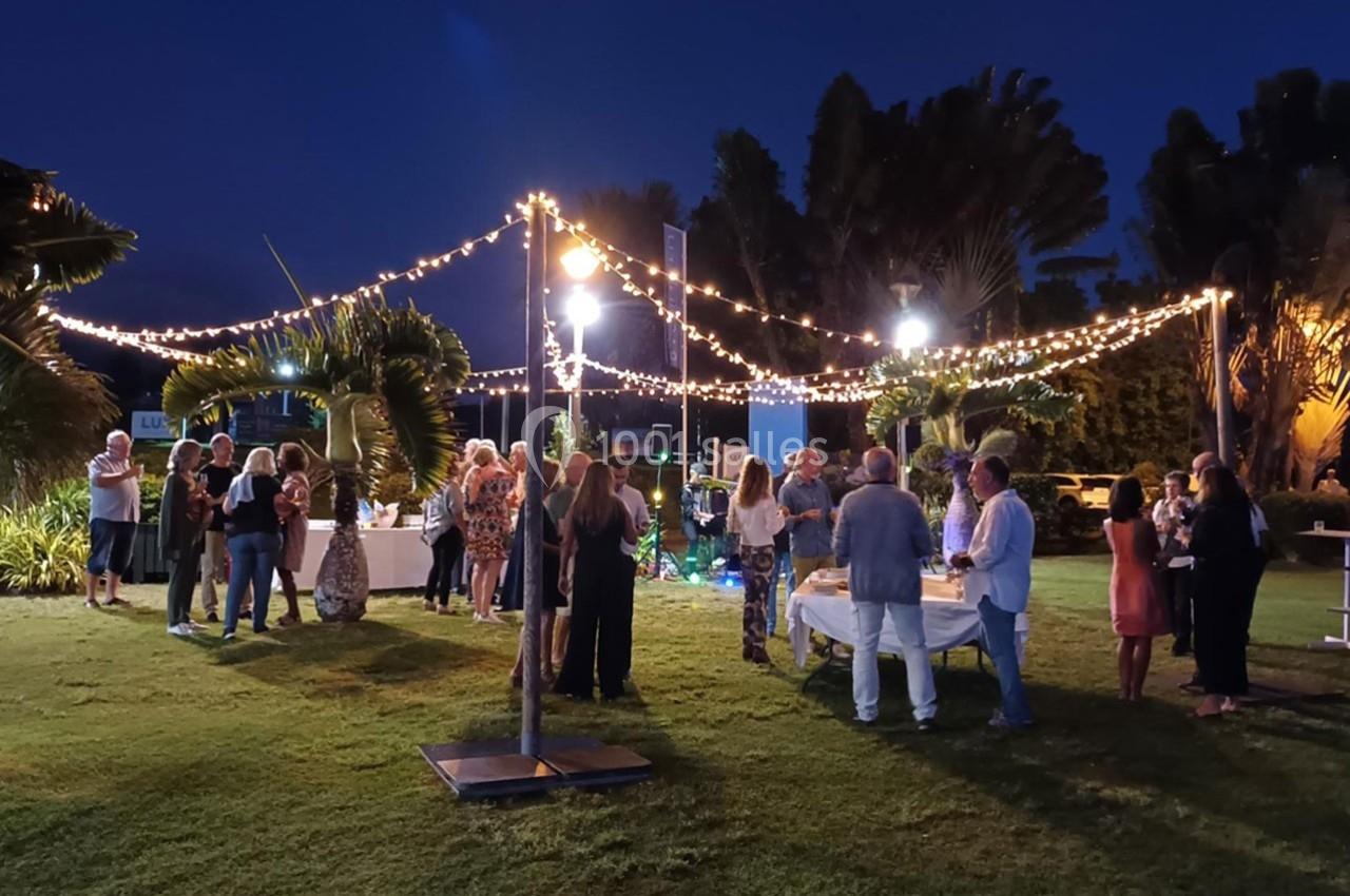 Groupe de personnes rassemblées dans un jardin éclairé par des guirlandes lumineuses en soirée.