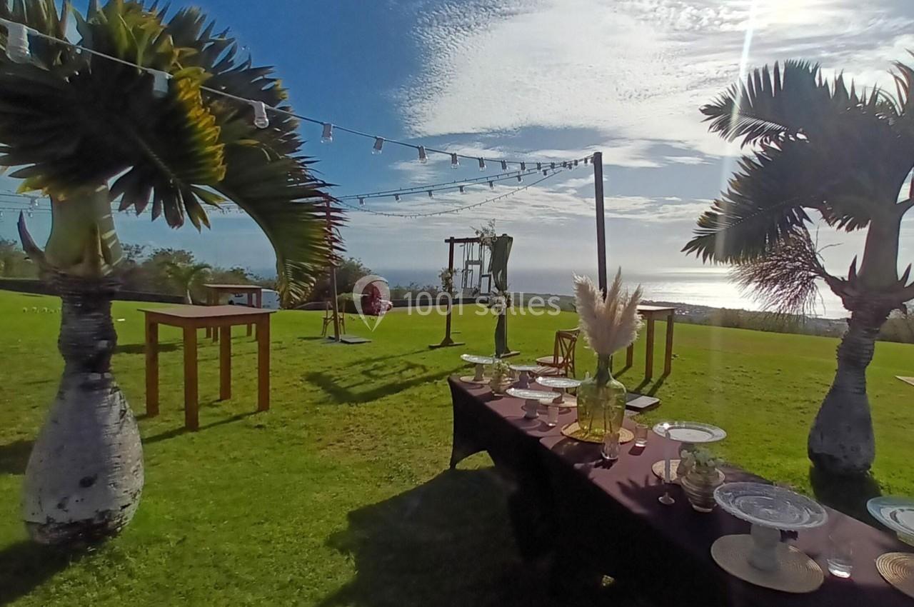 Table dressée en extérieur avec vue sur la mer, entourée de palmiers et décorée pour un événement en plein air.