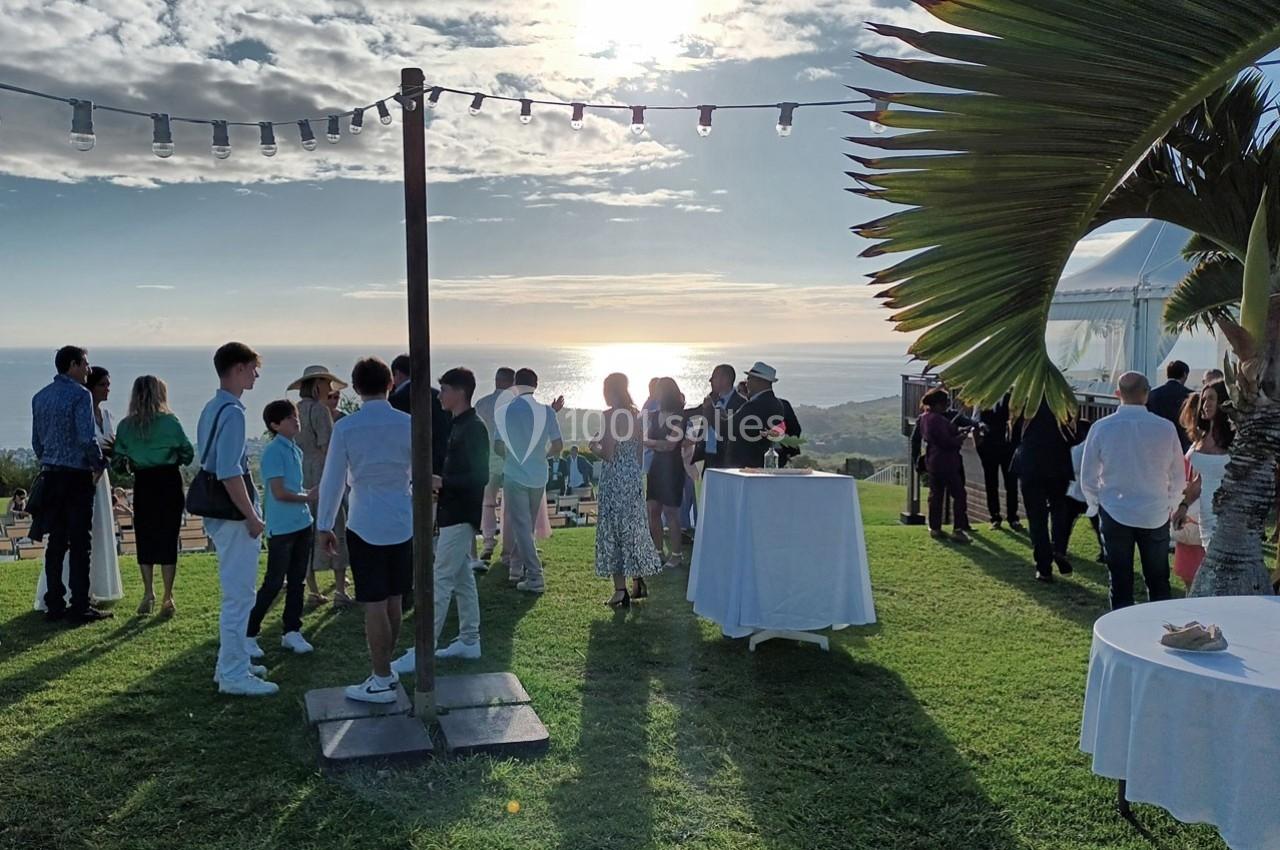 Groupe de personnes rassemblées en extérieur sur une pelouse, au coucher du soleil, près de la mer.