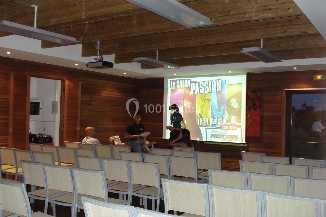 Salle de conférence vide avec des chaises alignées, un projecteur affichant une présentation et trois personnes discutant.