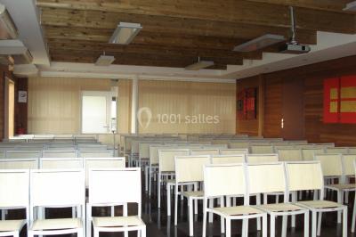 Salle de conférence vide avec des rangées de chaises blanches et un plafond en bois.