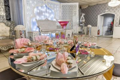 Salle de réception élégante avec tables dressées, chaises transparentes et lustres suspendus sous un plafond drapé.