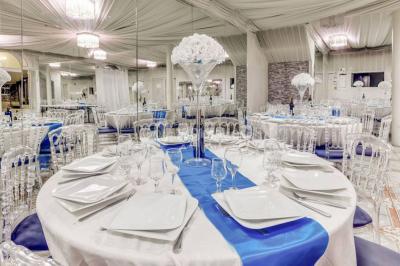 Salle de réception élégante avec tables dressées, chaises transparentes et lustres suspendus sous un plafond drapé.